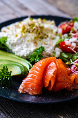 Breakfast - smoked salmon, cottage cheese, avocado and vegetable salad on wooden table
