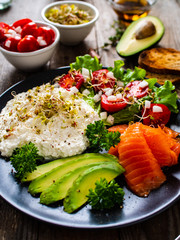 Breakfast - smoked salmon, cottage cheese, avocado and vegetable salad on wooden table
