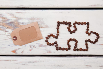 Puzzle piece of coffee beans and blank tag. White wooden planks.