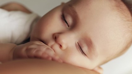Close-up portrait of peaceful sleep baby boy in mother arms.