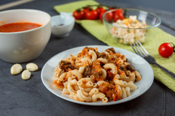 Close up view of pasta with meat and tonato sauce in the front. Tomato soup and colorful salad in the background. Lunch surving example. Homemade tasty and nutritious food. 