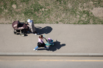 Women with a baby stroller and child on a toy bike walking towards each other, top view. Quarantine...