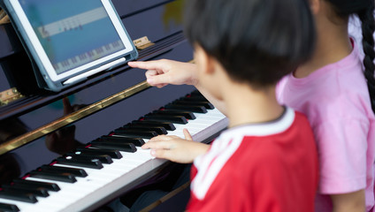 children play piano together with tablet learning at home education online in covid 19 crisis