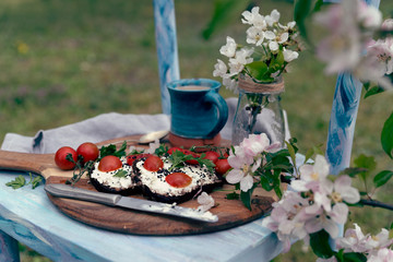 Rural breakfast in the garden on chair with blooming flowers and homemade slice of bread and tomatoes and mug of coffee in blue color. Healthy natural food outdoors. Close up.
