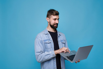 Young cheerful man with laptop in his hand. Guy browsing internet on computer and expresses happiness. Blue background. Free space for text.