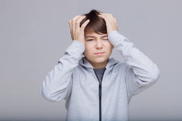 Sad boy holds his head. Teenager feeling sick, having headache.