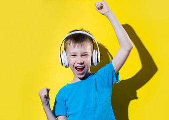 Boy having fun and dancing while listening music using earphones isolated over yellow background.