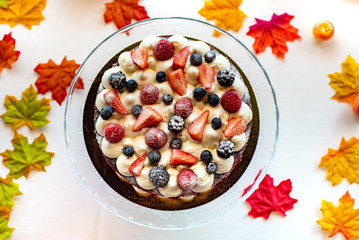 Delicious tart with fresh strawberries, raspberries and currants on the table. Top view horizontal. Against the background of autumn leaves