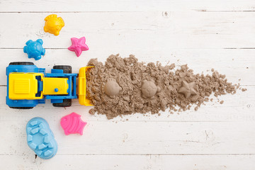 A tractor with a bucket removes kinetic sand from the table. Top view on colorful sand molds and...