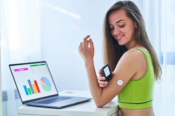 Woman suffering from diabetes using remote sensor and computer for control, monitoring and examining glucose blood levels diagrams and graphs. Diabetics lifestyle and healthcare