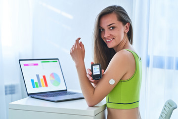 Woman suffering from sugar diabetes using remote sensor and computer for control, monitoring and examining glucose blood levels diagrams and graphs. Diabetics lifestyle - obrazy, fototapety, plakaty
