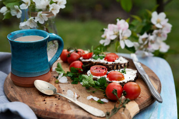 Healthy vegetarian breakfast with mug of coffee in the garden with fruit tree and flower in rustic style. Food in the morning with sandwich, tomato and parsley on a rural table. Summer background.