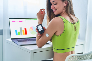 Woman suffering from diabetes using remote sensor and computer for control, monitoring and examining glucose blood levels graphs. Diabetics lifestyle and healthcare - obrazy, fototapety, plakaty