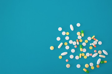 Colorful pills and capsules on a blue green background, tablets are scattered from the lower right to the center of the image, with a free area for text