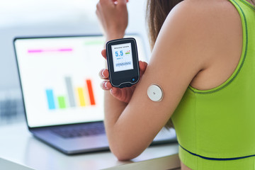 Diabetic patient using remote sensor and laptop for control and online monitoring glucose blood levels graphs. Medical technology in diabetes treatment and healthcare - obrazy, fototapety, plakaty