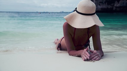 Beautiful woman on holiday relaxing lying on the beach wearing straw hat. Holiday and travel concept