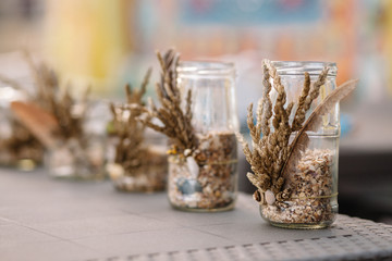 The glass jars is decorated with feathers, ears of grass and shells. Decoration on the wedding table. Rustic wedding.