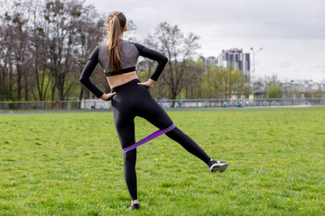 Obraz na płótnie Canvas Fitness girl exercising with fitness gum bands in black tracksuit outdoors