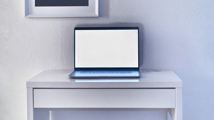 Laptop with blank display at the workspace in a white interior. Mockup and space for text and advertising