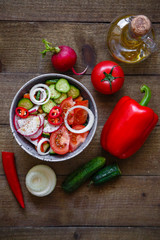 Salad of tomatoes cucumbers onions radishes avocado peppers on a wooden background.