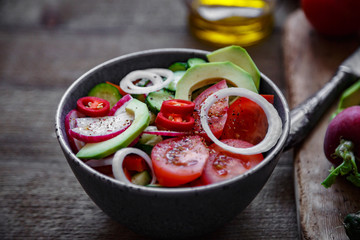 Salad of tomatoes cucumbers onions radishes avocado peppers on a wooden background.