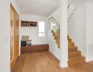 Foyer in white and bright new home with hardwood floors, stairs, bench, and front door. 