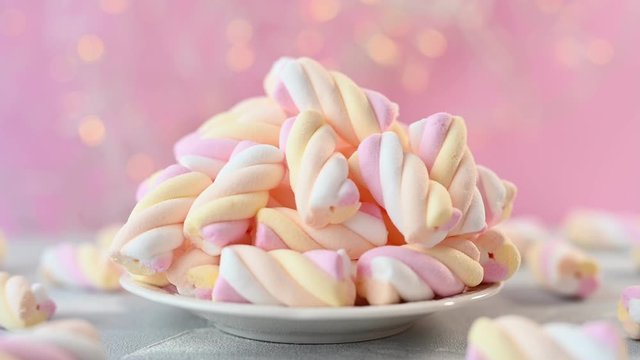 marshmallows of pink yellow and white colours lie on plate in coffee shop with flashing lights on wall close view
