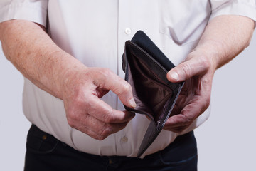 An elderly man holds an empty wallet in his hands. The concept of poverty, job loss, dismissal, retirement, price increases.