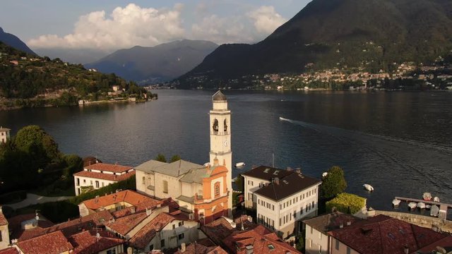 Aerial view of Saint Vincent Church in Cernobbio. Panoramic shooting from a drone on a summer sunset day. A flock of birds flies over the roofs of houses