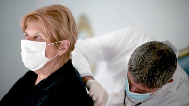 Doctor Using Stethoscope For Auscultate Caucasian Elderly Female Patient With Face Mask At Home. Life Insurance, Healthcare With Long Live, Coronavirus Prevent Epidemic