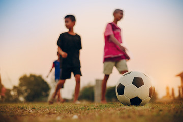 Fototapeta premium Action sport outdoors of kids having fun playing soccer football for exercise in community rural area under the twilight sunset sky.