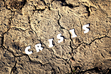 The word CRISIS in paper letters on the background of dry earth with cracks. Crisis concept.