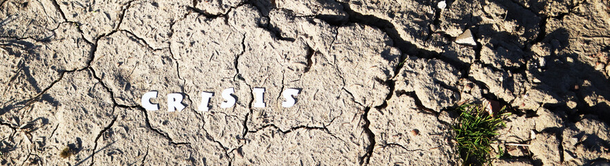 The word CRISIS in paper letters on the background of dry earth with cracks. Crisis concept. Banner.