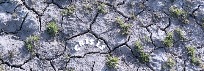 The word CRISIS in paper letters on the background of dry earth with cracks. Crisis concept. Banner.
