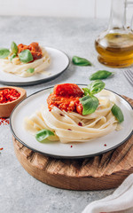 Pasta Tagliatelle Bolognese with meat tomato sauce and fresh basil leaves on white plate and wooden cutting board. Light gray table.