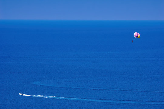 Parasailing water amusement. Flying on a parachute behind a boat on a summer holiday by the sea in the resort. Beautiful bright blue water and colorful parachute.