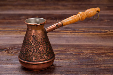 Close up decorative turkish coffee pot on wooden table. Long wooden handle. Brown rustic wood.