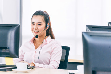 Asian woman call center with headset sitting at office desk working overtime. happy female employee...
