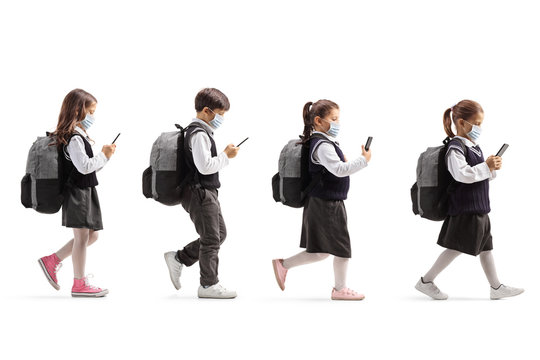 Schoolchildren with protective face masks walking in line and holding mobile phones