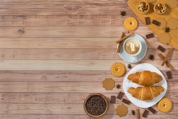 Rustic wooden background with cup of coffee, croissants, cookies and chocolate. Breakfast at morning. Top view, place for text.