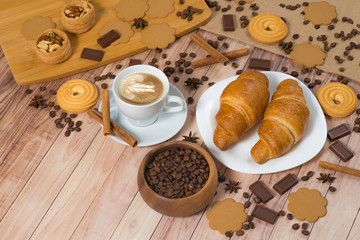 Close up coffee cup, croissants with coffee beans, cookies and chocolate on rustic background, top view