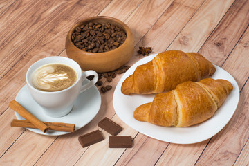 Coffee cup with croissants, chocolate, coffee beans and cinnamon on wooden background. Latte art.
