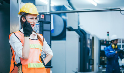 serious woman manager engineer in safety uniform using walkie talkie radio phone calling team worker, coworker working on machine technology invention industry manufacturing factory at background