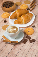 Coffee cup with croissants, cookies, chocolate and coffee beans on wooden background. Latte art. Space for text