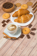 Coffee cup with croissants, cookies, chocolate and coffee beans on wooden background. Latte art. Space for text