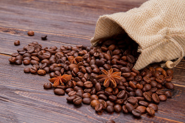 Coffee beans and anise spillen out from bag. Rustic wooden surface.