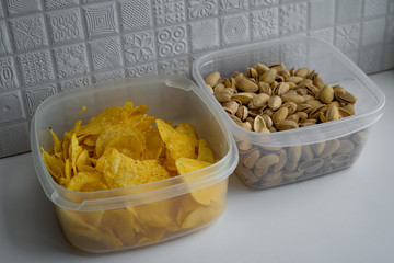 Side closeup view of delicious crispy snacks such as salted dry pistachio nuts and potato chips which are stored in plastic transparent containers