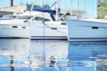 White modern sailing boats (for rent) moored to a pier in a yacht marina on a clear summer day....