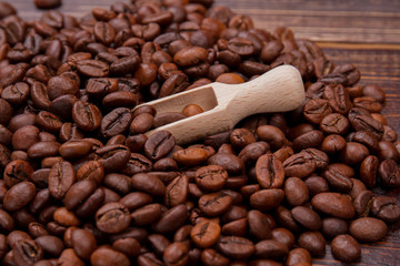 Close up small wooden spoon or scoop with coffee beans. Short wooden scoop and brown grains.