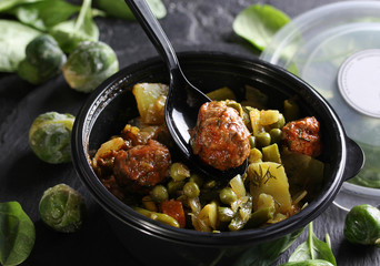 Healthy green food. Stewed cabbage, potatoes, peas and meatballs in a black plastic bowl with a spoon. Green brussels sprouts, spinach on a black background. Background image, copy space